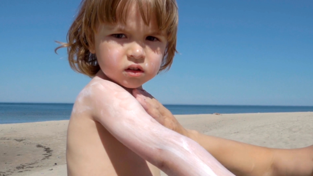 Detetu na plaži odrasla osoba maže ruku kremom za sunčanje