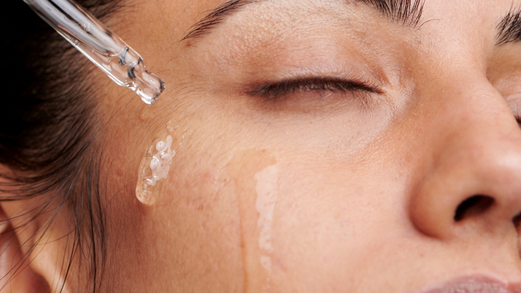 Žena zatvorenih očiju nanosi providan serum pipetom na lice