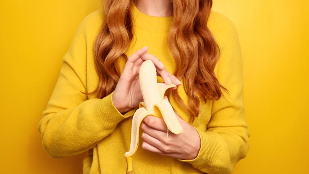 Devojka u žutom džemperu ljušti bananu