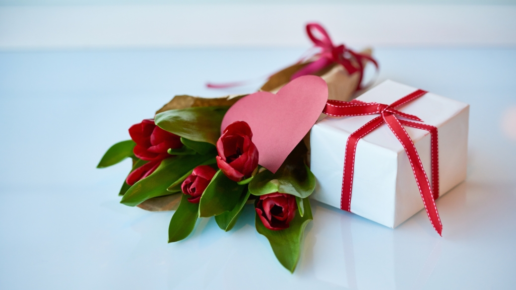 Bela poklon kutija sa crvenom mašnom, buket cveća i ružičasto srce na svetloj podlozi