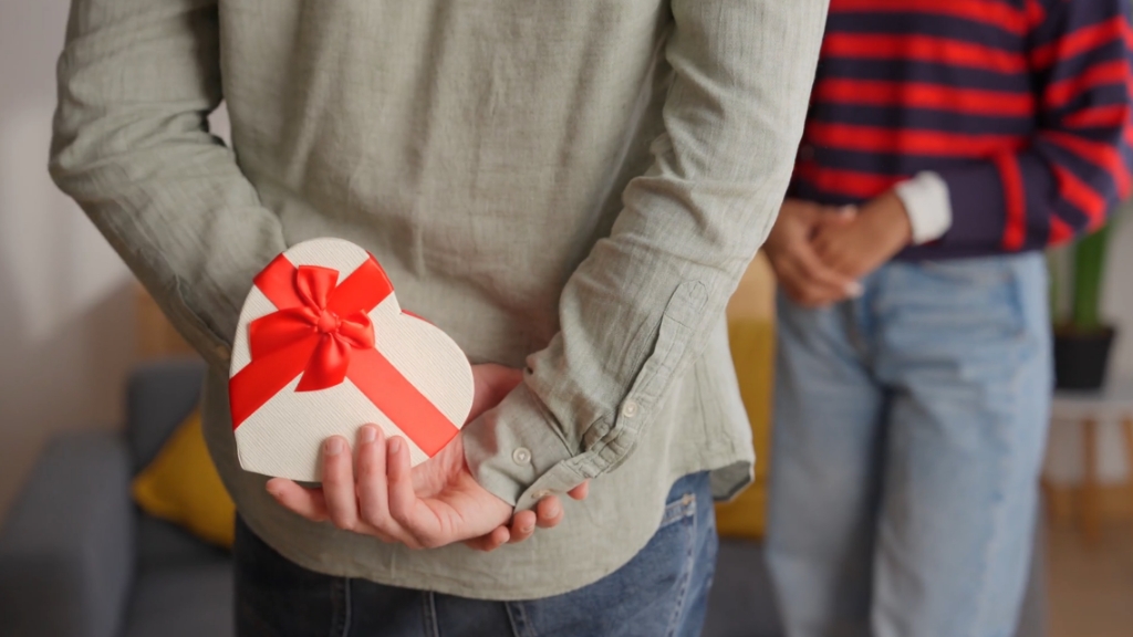 Muškarac drži poklon za Dan zaljubljenih iza leđa, dok stoji ispred žene