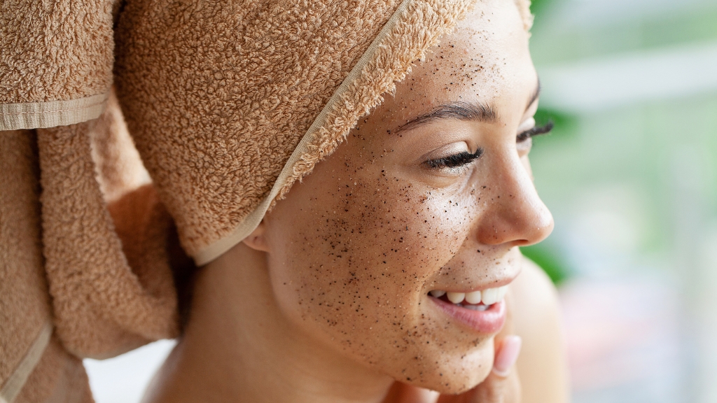 Žena sa peškirom na glavi nanosi piling na lice