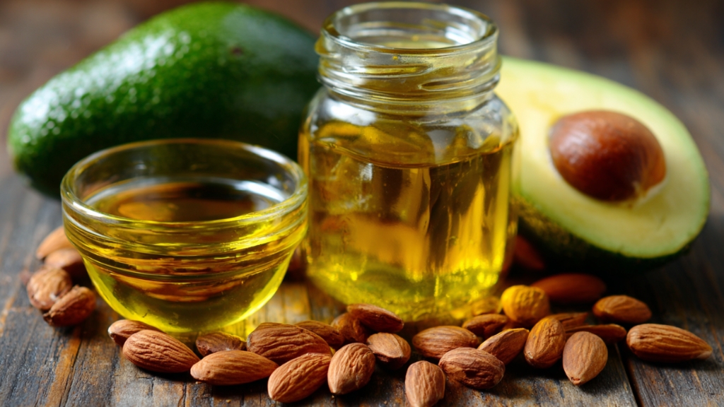 Maslinovo ulje u staklenim posudama, avokado presečen na pola i bademi poređani na drvenom stolu
