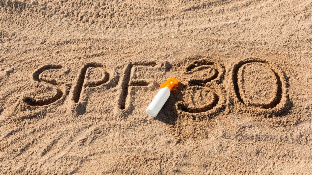SPF 30 je ispisan u pesku pored kreme za zaštitu od sunca na plaži