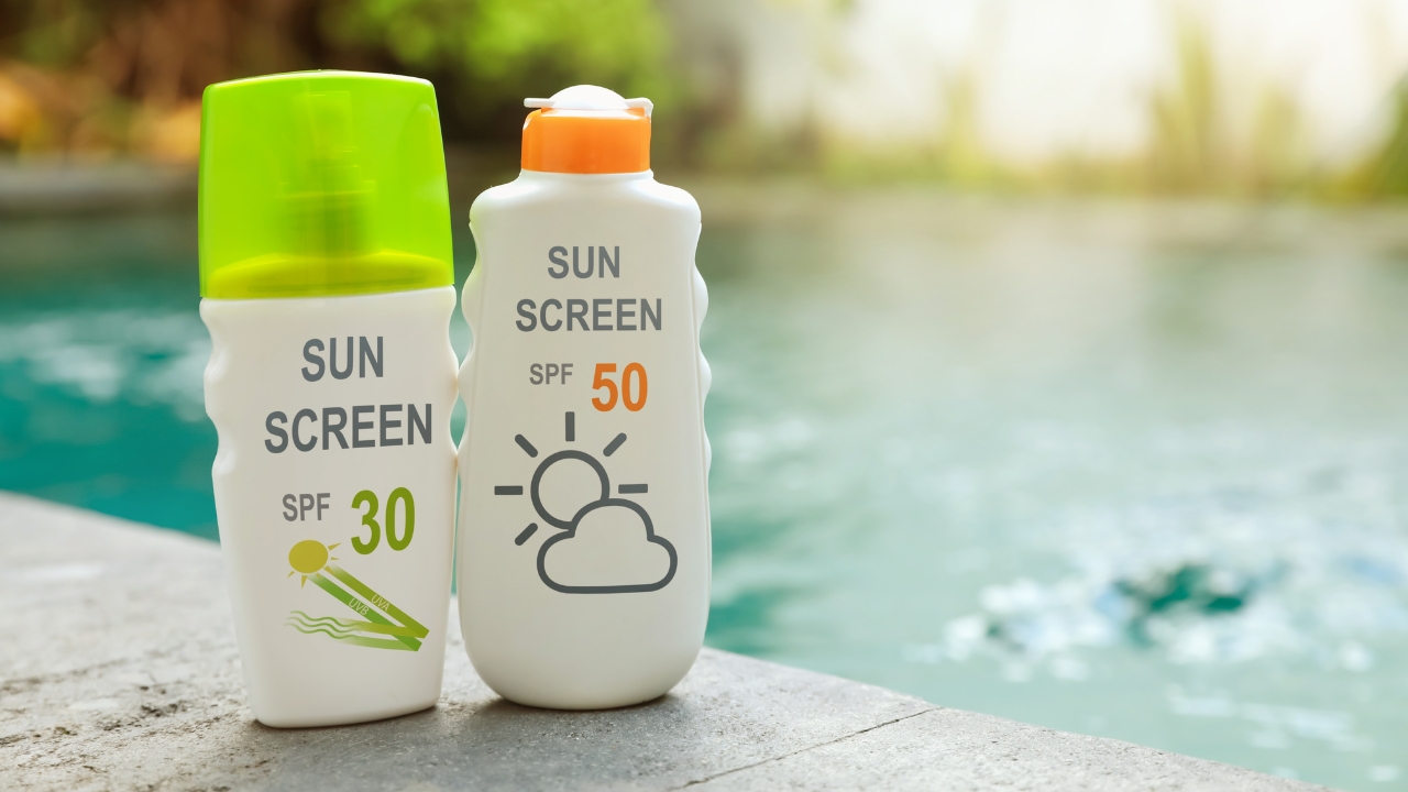 SPF 30 i SPF 50 kreme za zaštitu od sunca stoje pored bazena tokom sunčanog dana